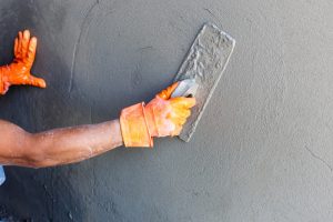 A man in an orange glove applying a sand render finish to a wall with a trowel.