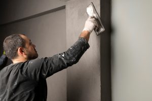 Professional plasterer applying the best render mix to a grey wall using a trowel, showcasing expert technique and high-quality workmanship in construction and wall finishing.