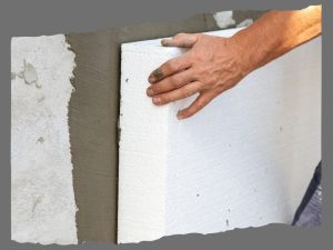 Hand installing white expanded polystyrene cladding on a building wall for insulation purposes.