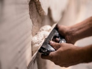 Wall cracks keep coming back? Expert applying plaster to a damaged wall.