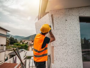 A worker installing polystyrene cladding panels on a building exterior, polystyrene cladding installation.