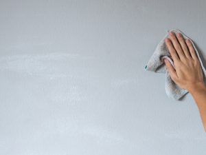 A hand wipes down a grey wall, likely preparing it for painting to avoid bubbling wall problems.