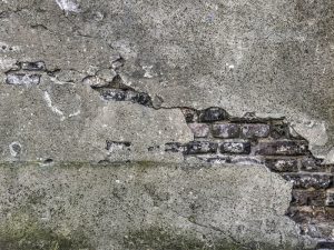 Cracked plaster wall showin' various crack patterns, exposin' the brickwork beneath.