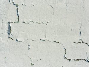 A close-up shows a white concrete wall with noticeable crack patterns across its surface.
