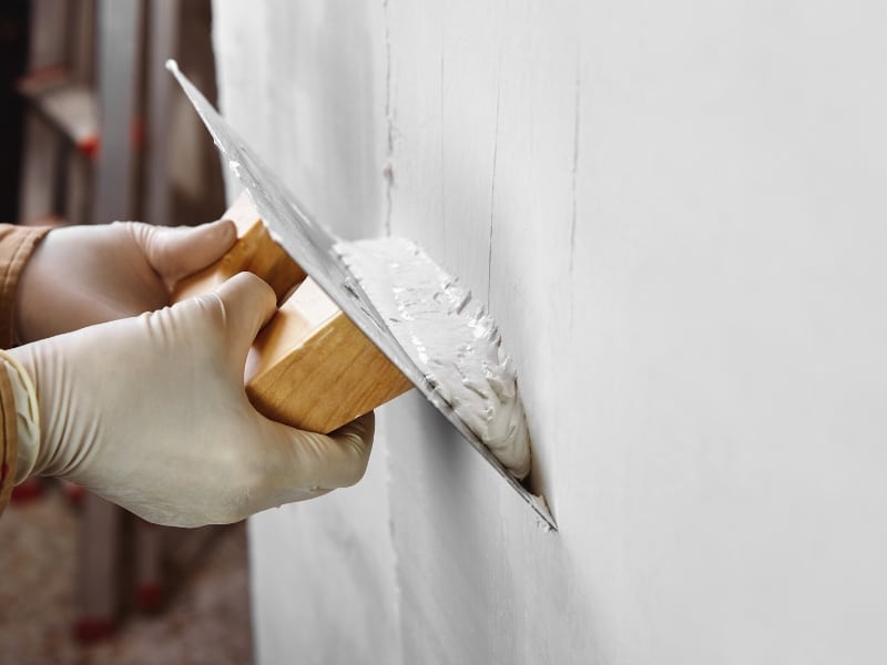 Trowel applying plaster to wall surface with existing cracked plaster walls