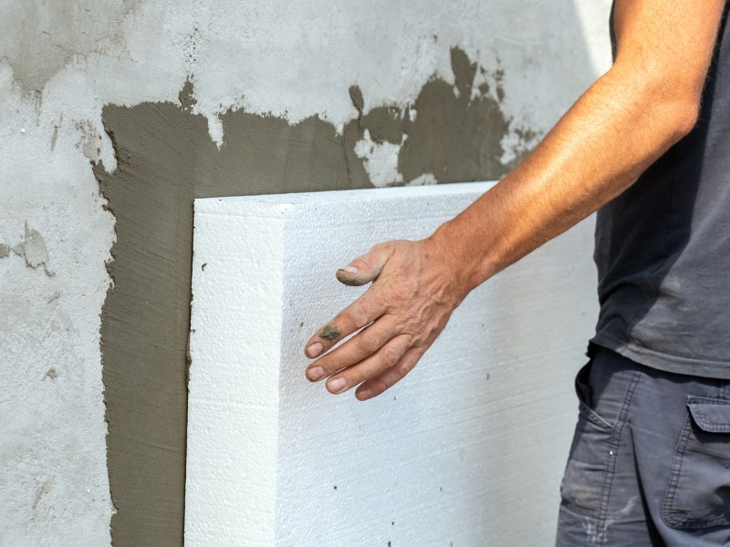 Worker installing polystyrene building material insulation panel on house wall. Worker installing polystyrene building material insulation panel on house wall.