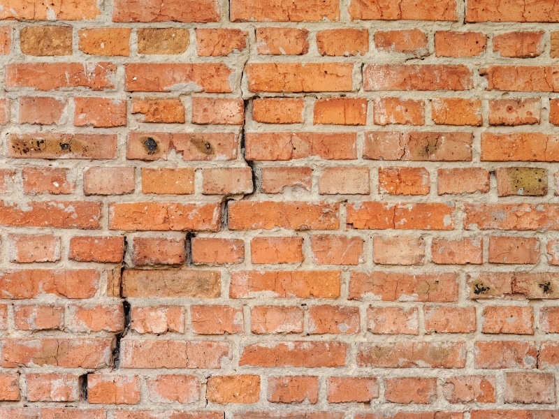 Cracks forming in a red brick wall showing early signs of structural damage needing fixing a cracked brick wall