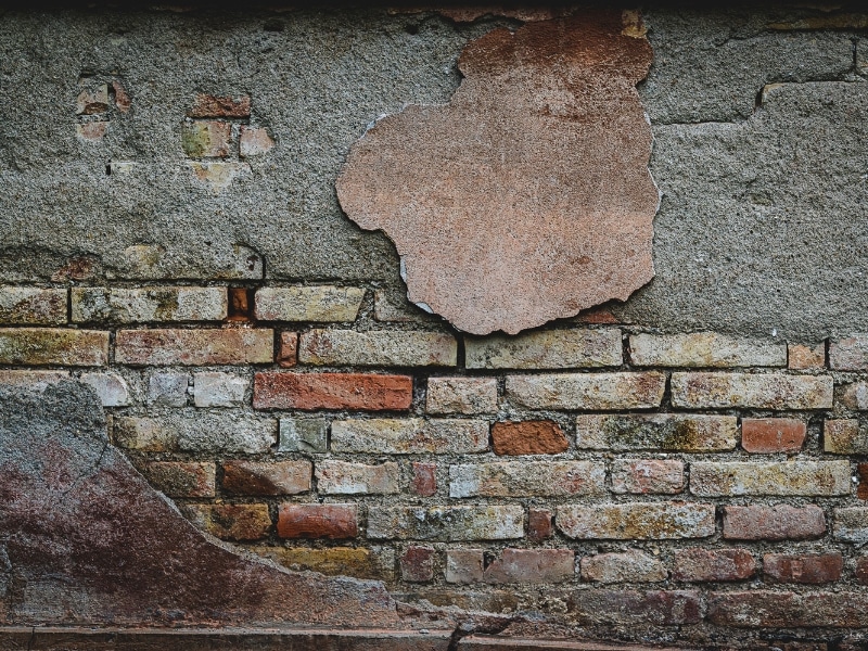 Old plaster peeling to reveal damaged bricks requiring fixing cracks in brick walls.