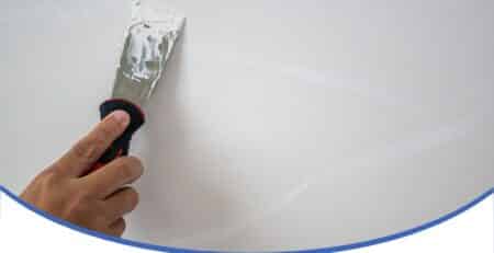 Hand applying concrete texture coating to a wall using a spatula for a smooth repair finish.