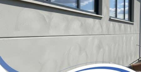 Exterior wall of a cement render house showing swirl marks and unfinished texture beneath windows on a sunny day.