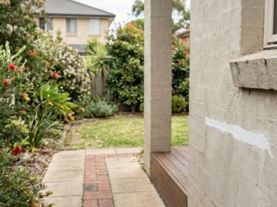 Homeowner patching a small render crack while a licenced renderer inspects the wall.