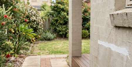 Homeowner patching a small render crack while a licenced renderer inspects the wall.